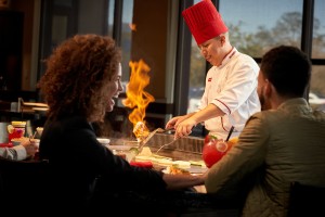 Couple smiles as they watch a Benihana chef cook with fire.