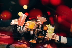 Four hands holding cocktails in cheers, in atmospheric glowing red lights