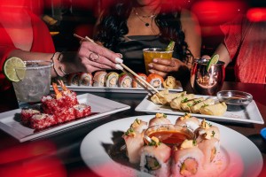 Person picking up dumplings with chopsticks, plates of delicious sushi surrounding