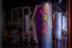 Licensee Enquiry Close-up view from outside a restaurant showing the STK logo on the window. Neon graphics are reflected in the glass. Interior columns and set dining tables are visible.